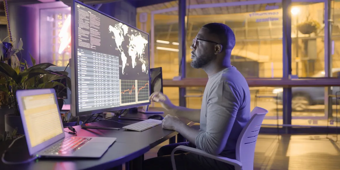 Data analyst reviewing global operations dashboards on a large curved monitor