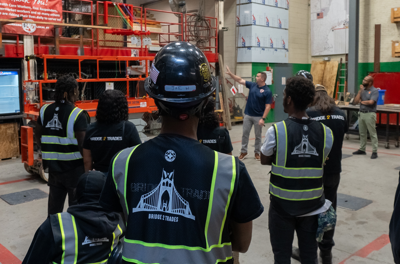 Young people in Bridge 2 Trades safety vests and hard hats touring a union training shop